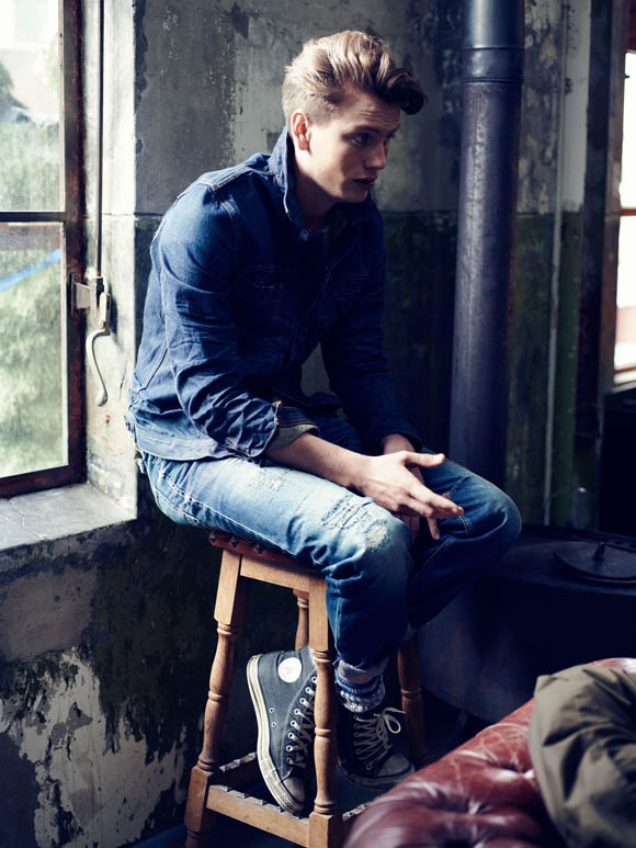 Young greaser gent sitting down on stool, grungy space + all denim